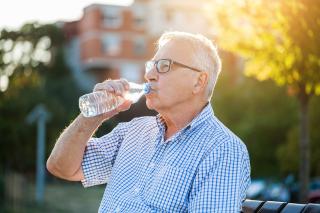 Elderly man relaxing on park bench drinking water